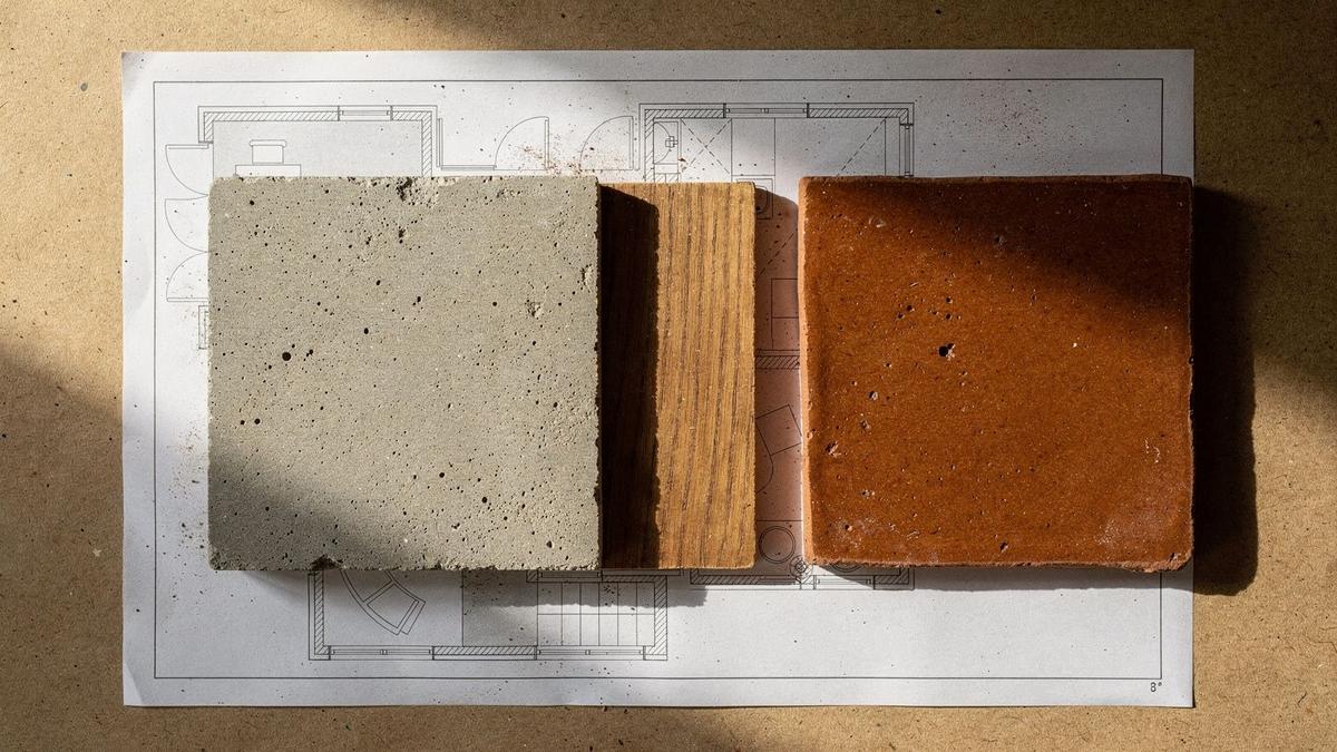 Finish samples of microcement, oiled oak and glazed tile laid over the printed M-04 material schedule on a drafting table